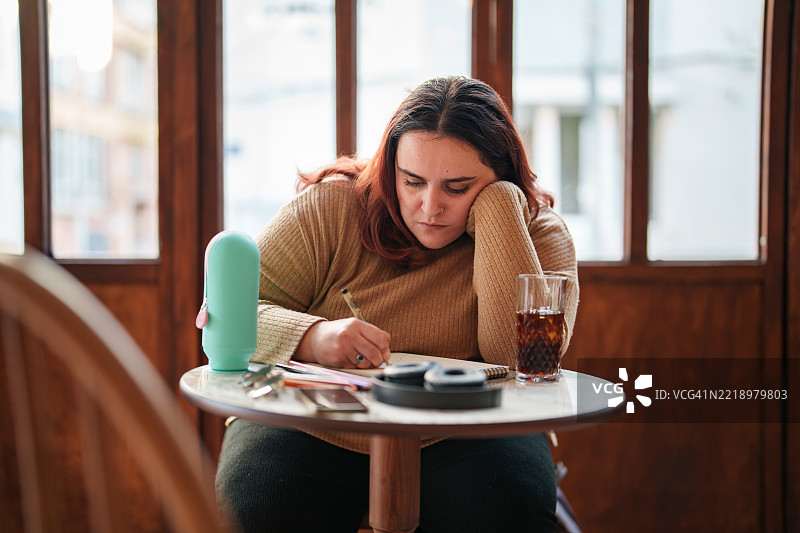 在咖啡馆用铅笔在素描本上绘画的女性图片素材