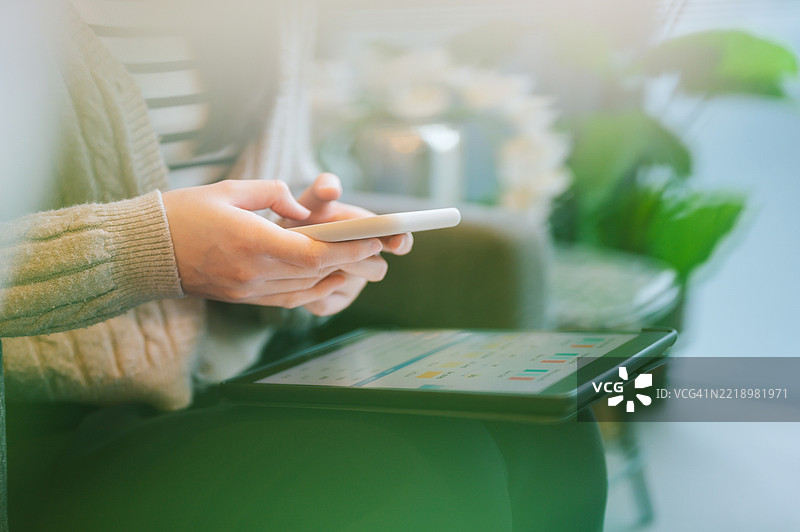 Z世代女性商务专业人士在多任务办公环境中使用智能手机，桌面上有笔记本电脑和文件，同时管理工作中的图表和报告。图片素材