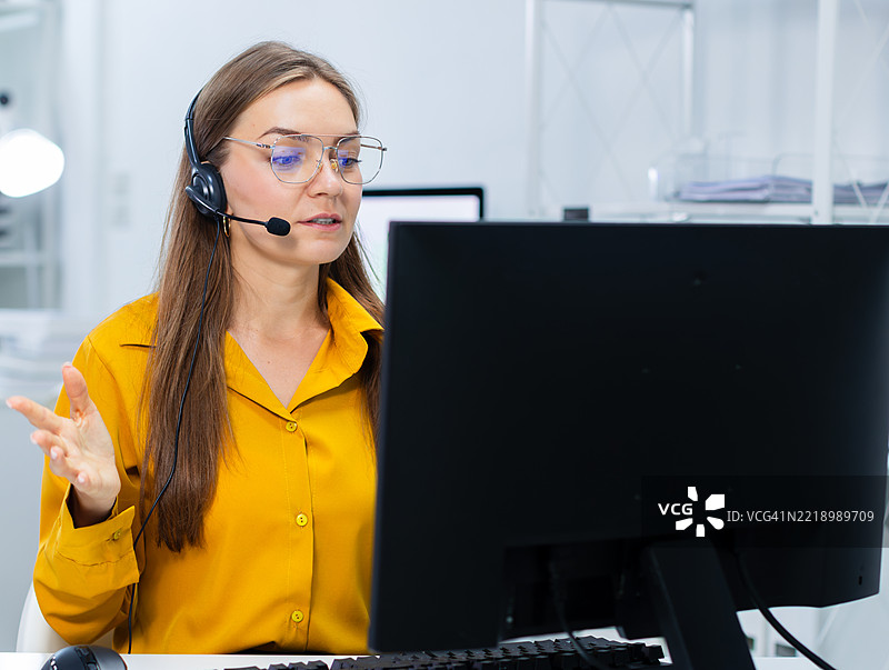 专业女性IT支持人员佩戴耳机，在现代办公室使用电脑工作图片素材