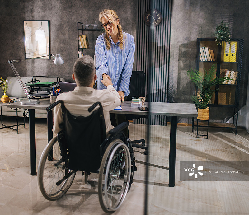一位坐在轮椅上的年轻人来到雇主面前寻找工作。图片素材