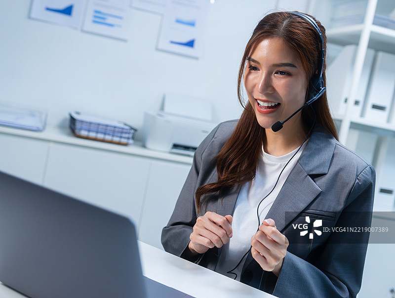 专业的亚洲女性IT专家与客户互动，佩戴耳机并使用电脑图片素材