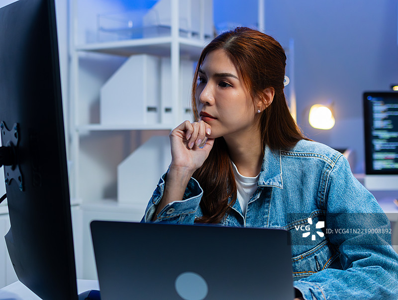 专业的亚洲女性软件工程师正在查看显示器屏幕，分析源代码算法图片素材