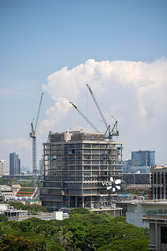 正在建设中的摩天大楼，塔吊矗立在已完工的高楼大厦之间，周围是绿意盎然的公园和蓝天。图片素材