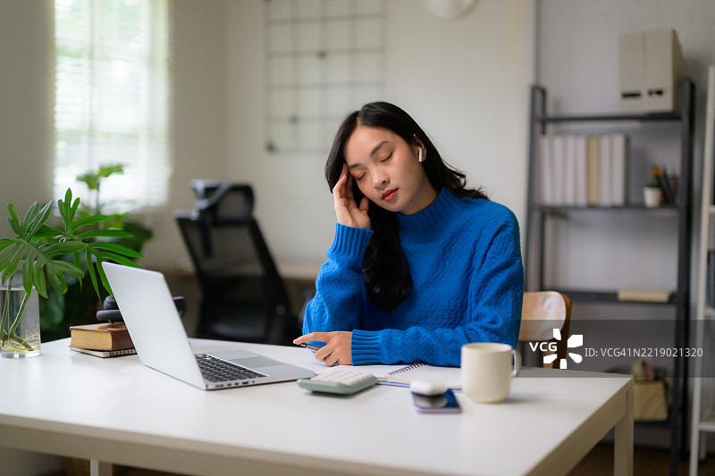 年轻的亚洲女商人因过度工作感到疲惫和压力，头痛并在家中使用笔记本电脑工作时休息。图片素材