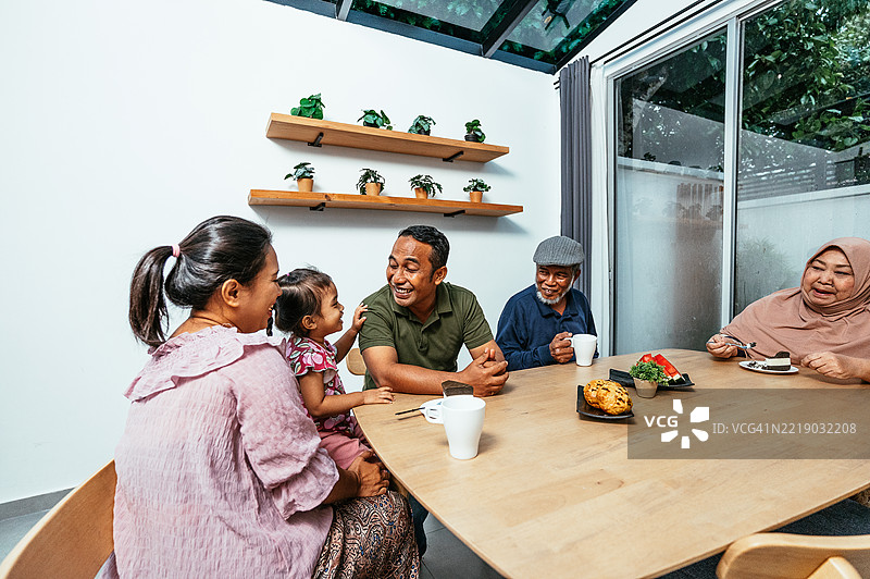 多代东南亚家庭在家享受一天，准备食物，吃零食和水果，和小女孩玩耍图片素材
