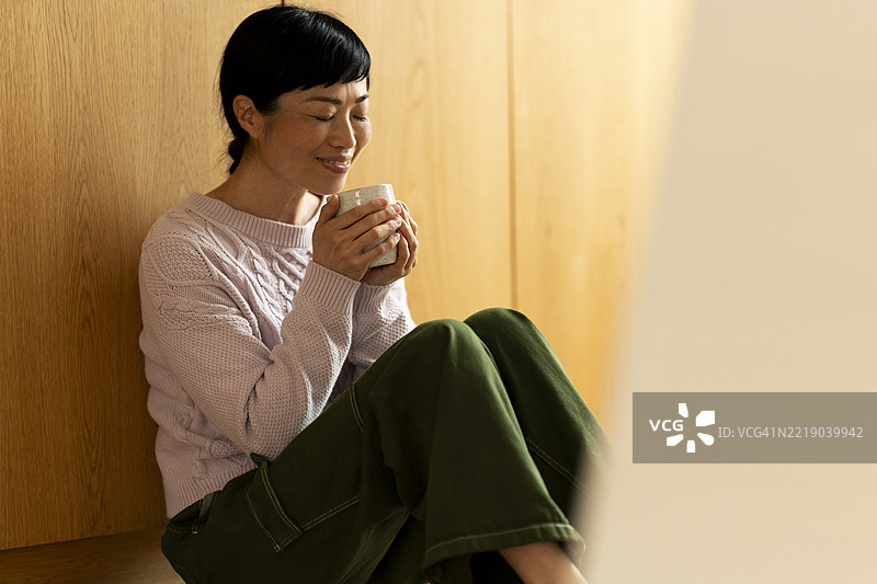 宁静的女性在家中享受一杯温暖的咖啡或茶图片素材
