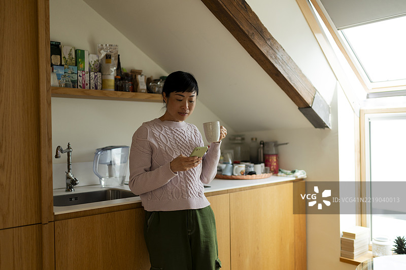 女人在厨房享受早晨咖啡并查看手机图片素材