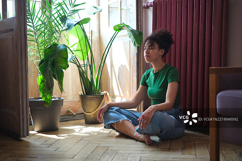 平静祥和的非裔美国千禧女性坐在莲花坐姿中，闭眼冥想以缓解家庭压力。年轻人的正念，心理健康。图片素材
