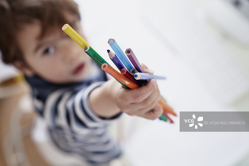 孩子手握五彩缤纷的蜡笔，专注于创作活动图片素材