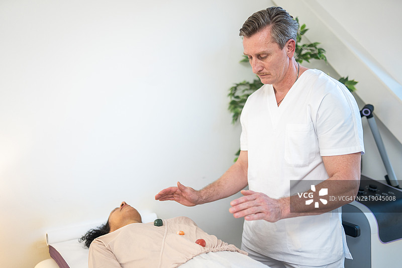 中年男性治疗师在明亮的室内环境中为放松的女性进行能量疗愈图片素材