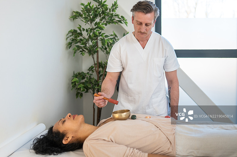 男性治疗师在明亮的自然光下为放松的西班牙裔女性进行声音疗法图片素材