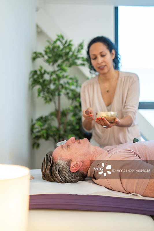 中年男性在放松疗法中，女性治疗师手持疗愈碗图片素材