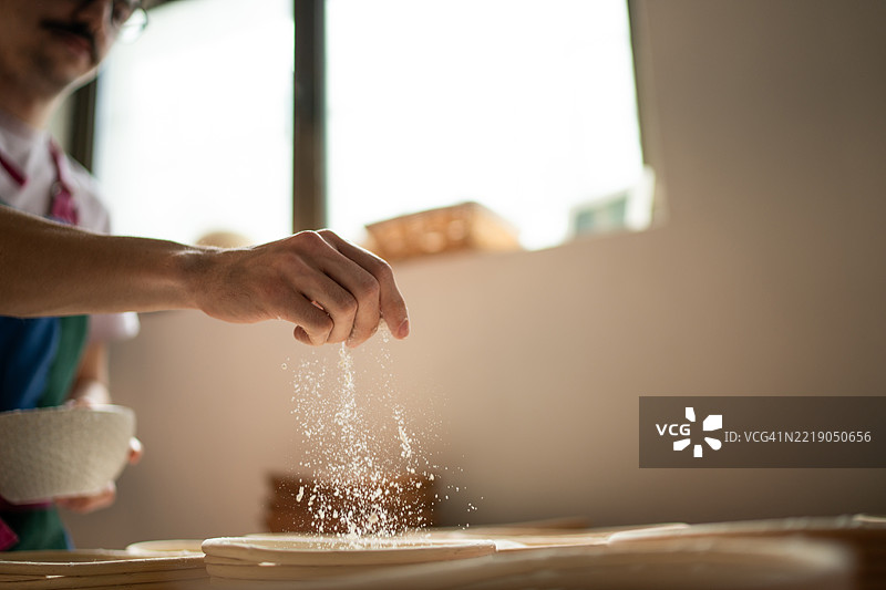 面包师在窗边向披萨面团撒面粉图片素材