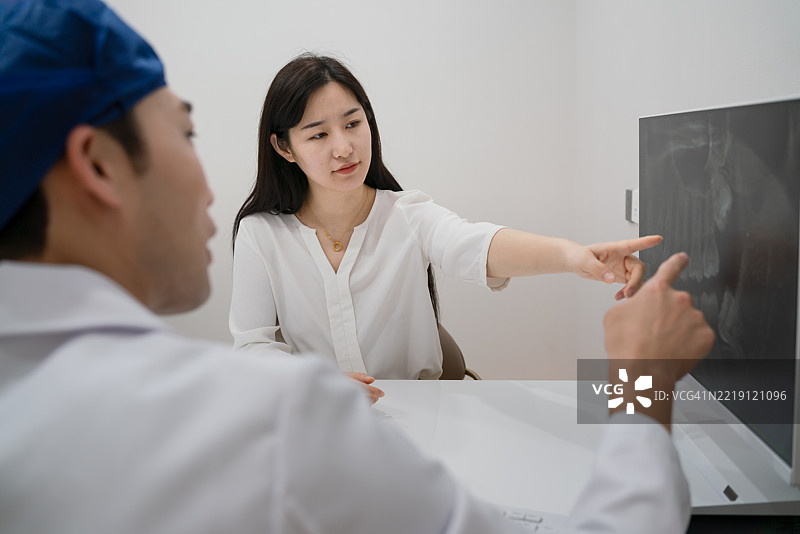 男牙医和女病人在诊所查看X光影像以讨论医疗计划。图片素材