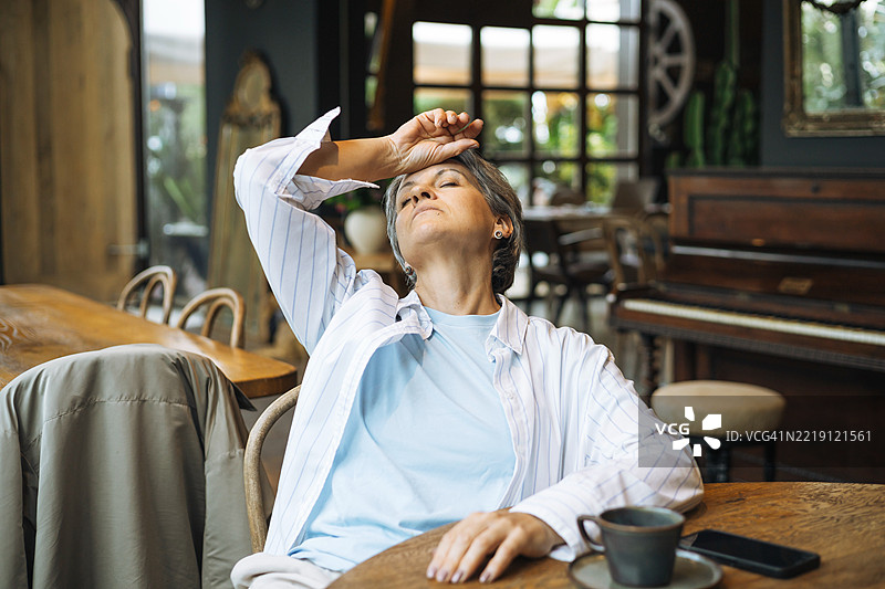 一位年长女性在咖啡馆的桌子旁放松，桌上有一杯咖啡和一部手机。图片素材