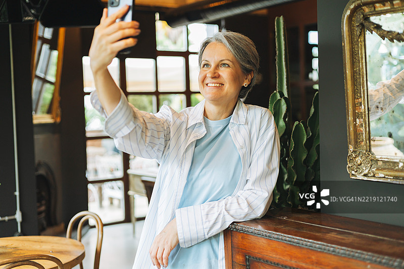 女性在舒适的咖啡馆或餐厅环境中微笑自拍。图片素材