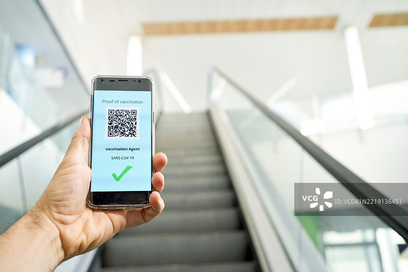 男子在机场手持显示疫苗接种证明的智能手机图片素材