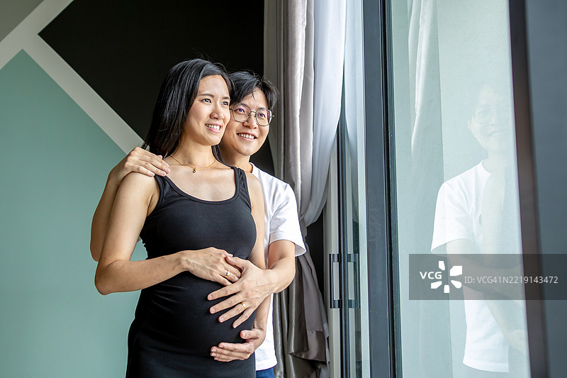 丈夫和怀孕的妻子站在窗边。图片素材