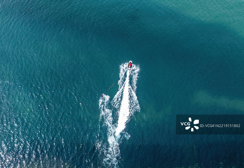 无人机航拍视角下，一人在海上滑水，身后是一艘摩托艇。图片素材