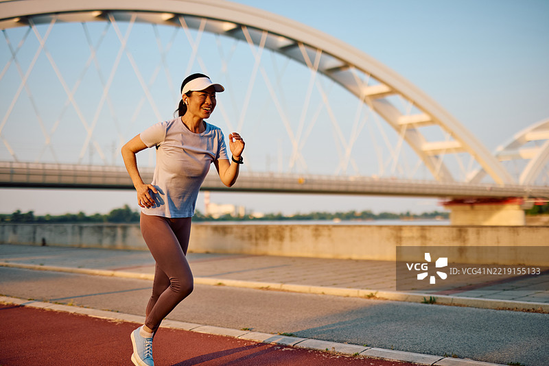 快乐的成熟的女性在河边慢跑，背景是桥。图片素材