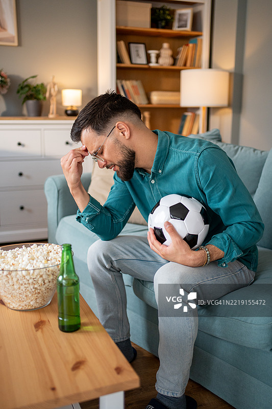 失望的足球迷在家里看足球比赛，手里拿着足球图片素材