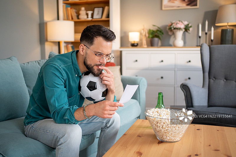 年轻男子在家观看比赛时查看足球投注图片素材