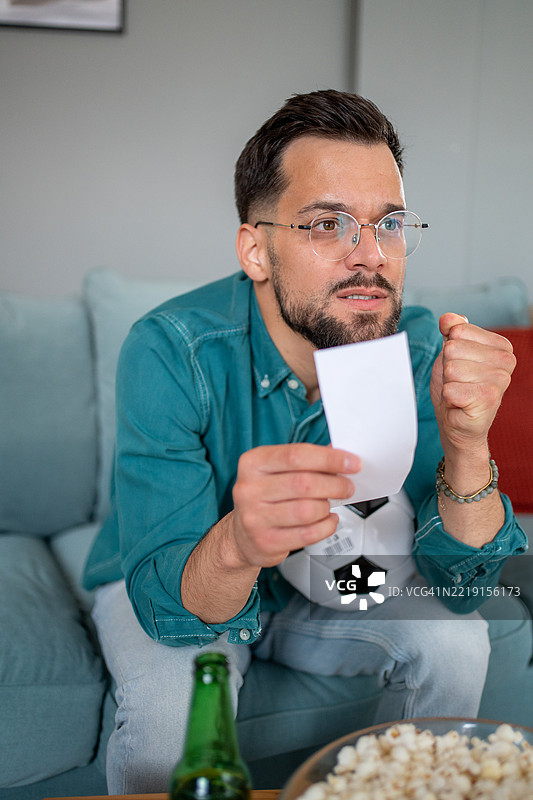 兴奋的体育迷在观看比赛，手里拿着投注单，旁边有啤酒和爆米花图片素材