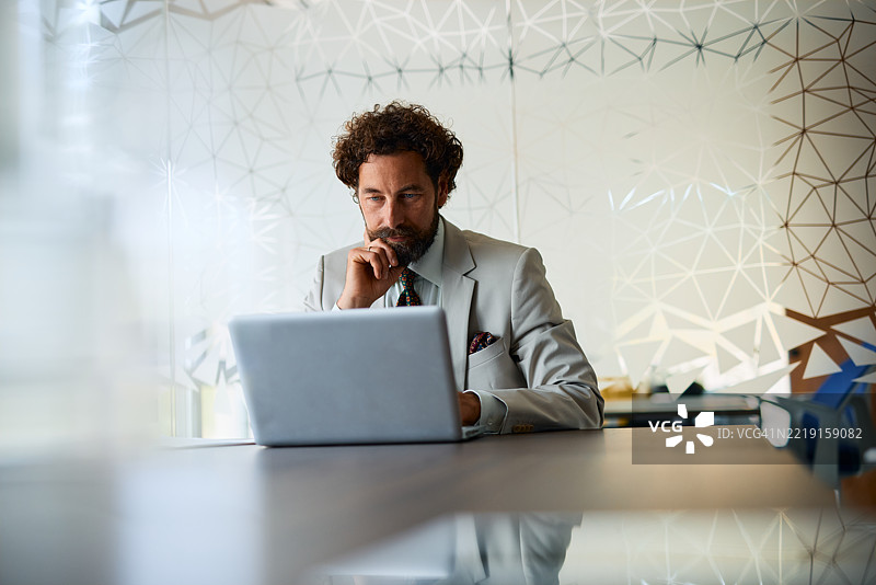 沉思的商人在现代办公室使用笔记本电脑图片素材