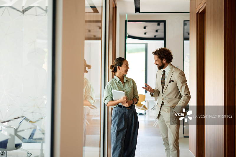 商务人士在现代办公室走廊交谈并微笑图片素材