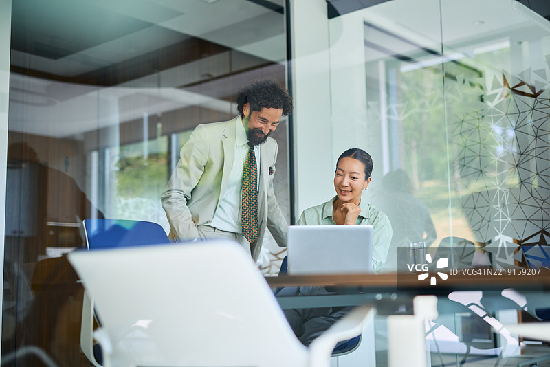 微笑的商务人士在现代办公室里一起使用笔记本电脑工作图片素材