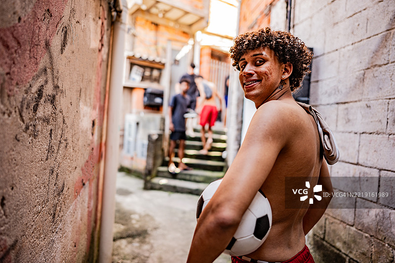 年轻的巴西足球运动员在小巷中回头看着足球图片素材