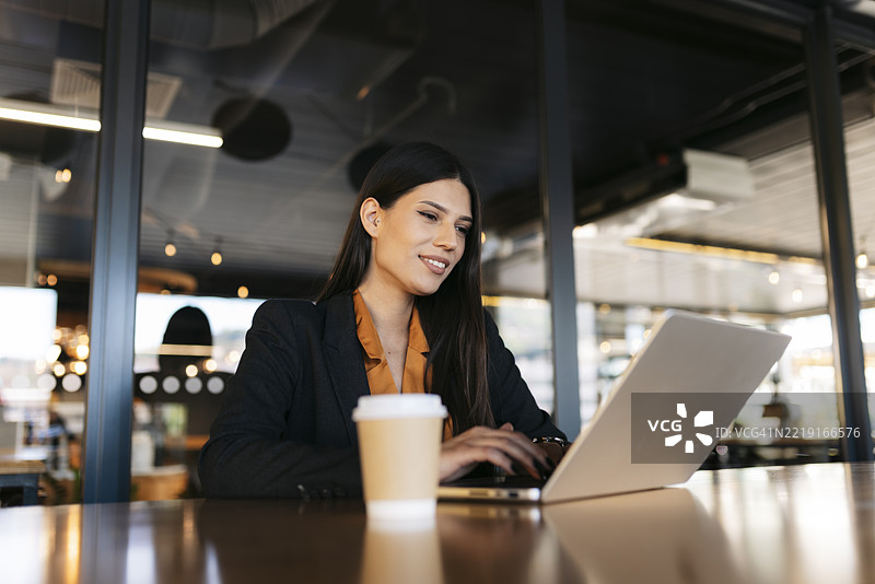 现代办公室里，商务女性正在用笔记本电脑工作，旁边有一杯咖啡。图片素材