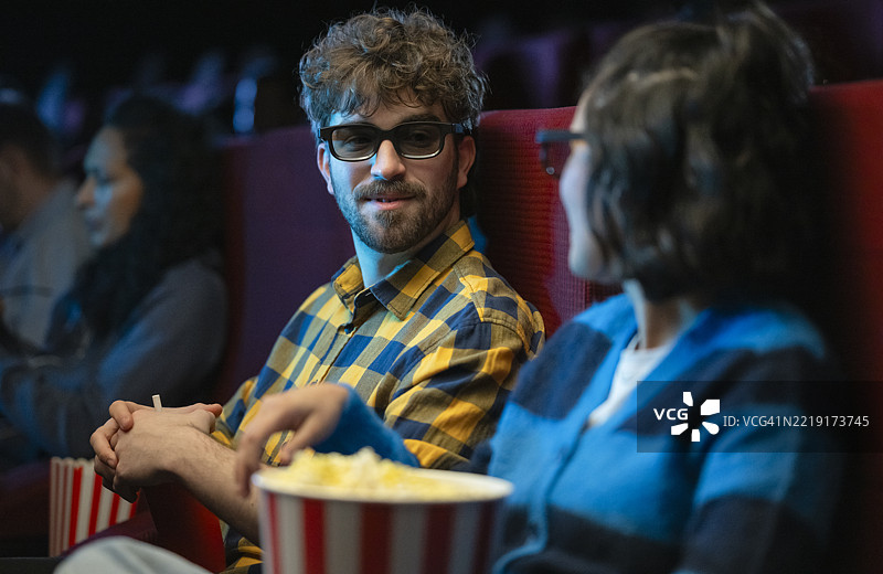年轻的多种族情侣在昏暗的电影院里享受3D电影和爆米花图片素材