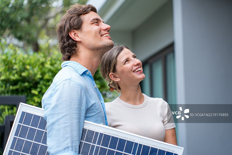 丈夫在住宅外与妻子讨论太阳能面板的安装。与家人一起咨询环保住宅。图片素材