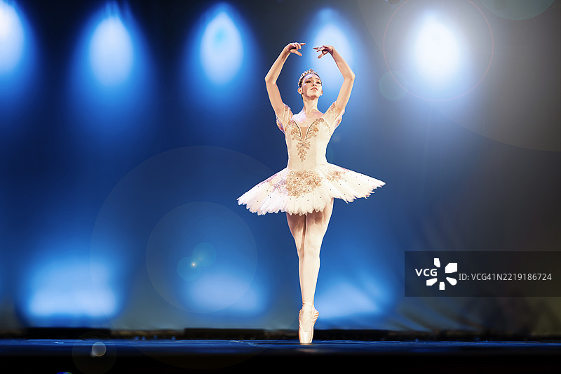 年轻女子在舞台上跳《雷蒙达》第一幕第三变奏，背景有大量镜头光晕。图片素材