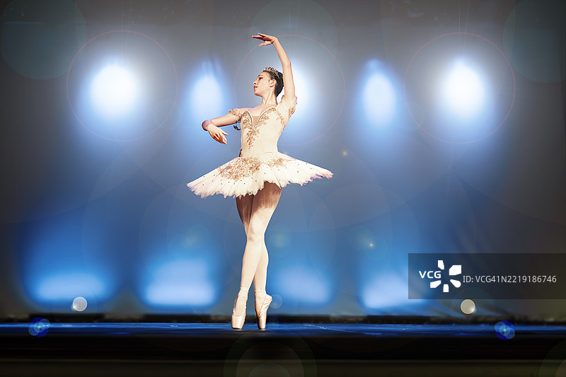 年轻女性在舞台上跳《雷蒙达》第一幕第三变奏，背景有大量镜头光晕。图片素材