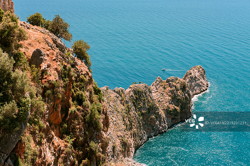 白天的原始海岸悬崖，碧蓝的海水和郁郁葱葱的绿植图片素材