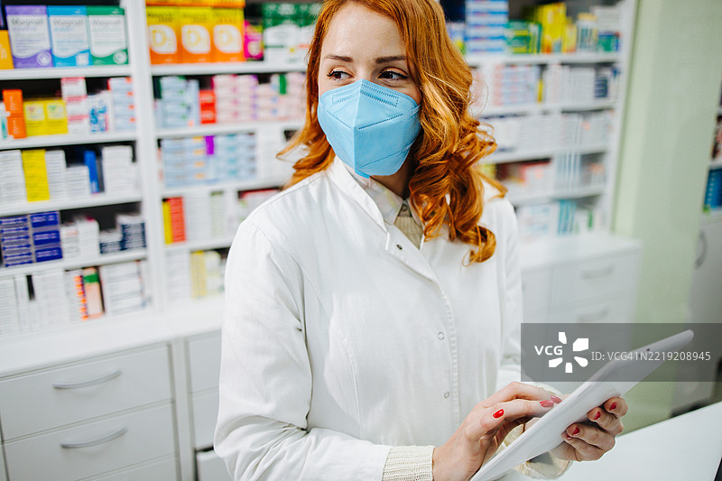 药剂师戴着外科口罩在药店使用平板电脑图片素材