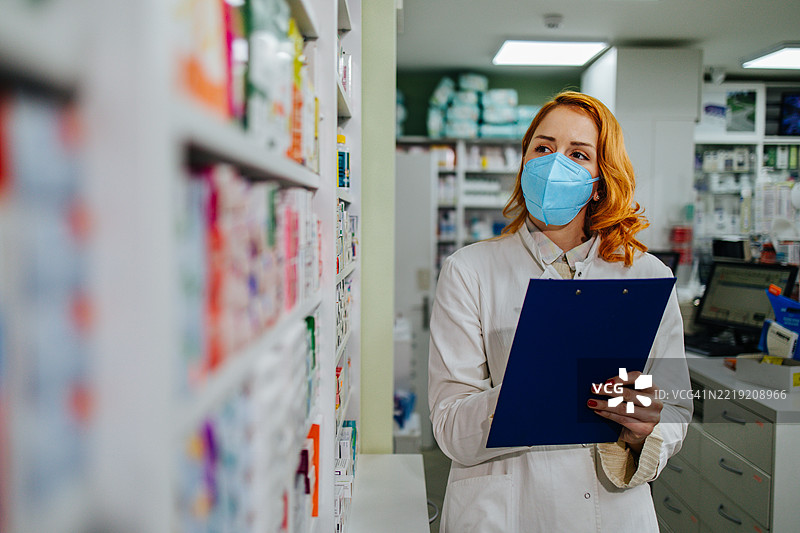 戴着外科口罩的药剂师在药店检查库存图片素材