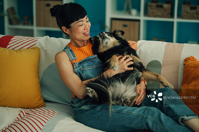微笑的女人在沙发上放松，抱着她的狗图片素材