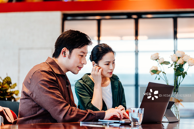 亚洲商务人士在咖啡馆的隔间里戴着耳机，使用笔记本电脑开会并共同工作。商务人士总是忙于使用笔记本电脑和手机。图片素材