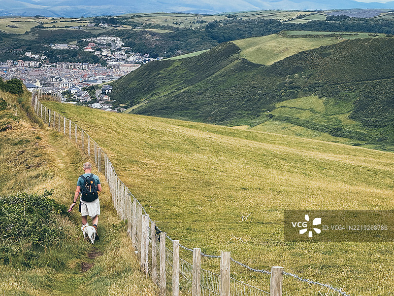 一名男子带着狗在前往阿伯里斯特威斯的塞雷迪根海岸小径上徒步旅行图片素材