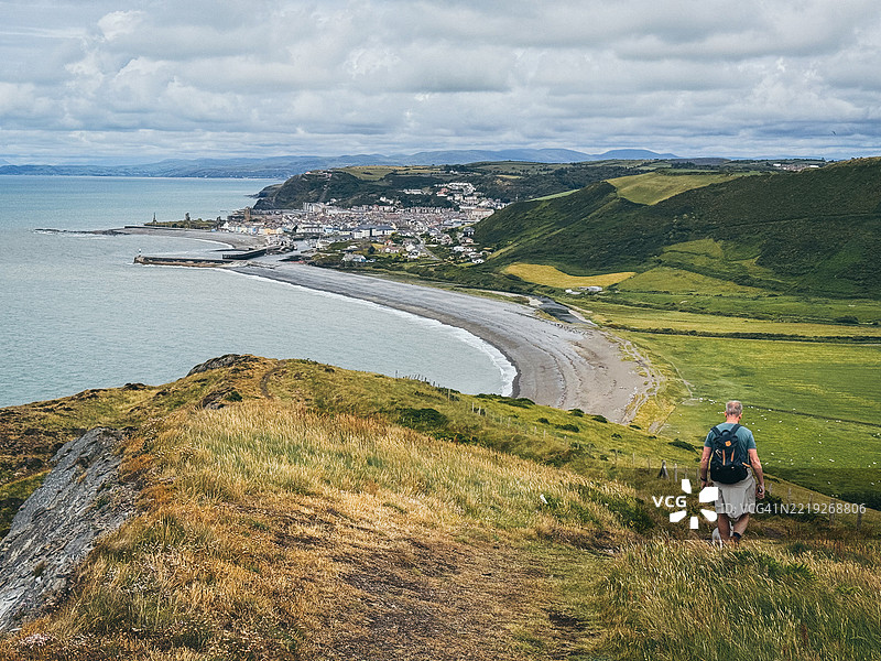 一名男子带着狗在前往阿伯里斯特威斯的塞雷迪戈恩海岸小径上徒步旅行图片素材