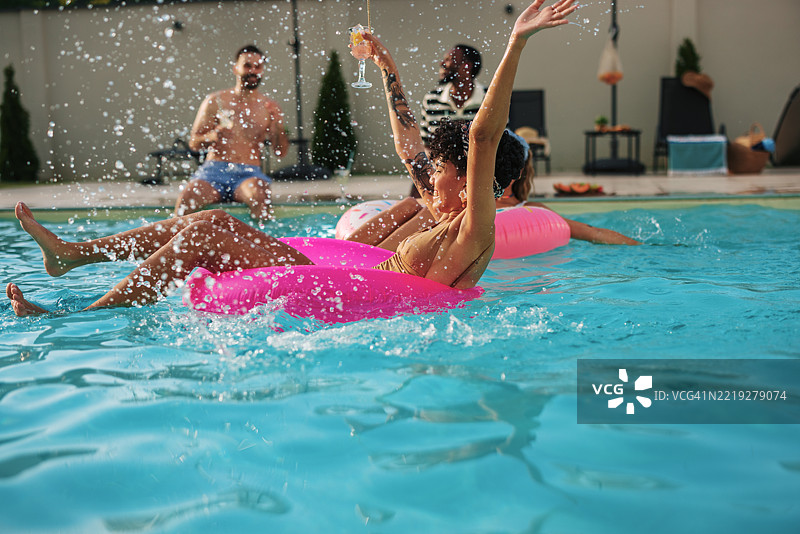 朋友们在游泳池里享受夏季假期，玩着充气圈图片素材