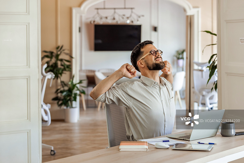男人在办公室的桌子前愉快地伸展双臂图片素材