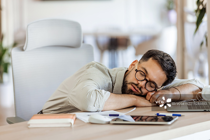 疲惫的员工在明亮的办公室环境中桌上睡觉图片素材