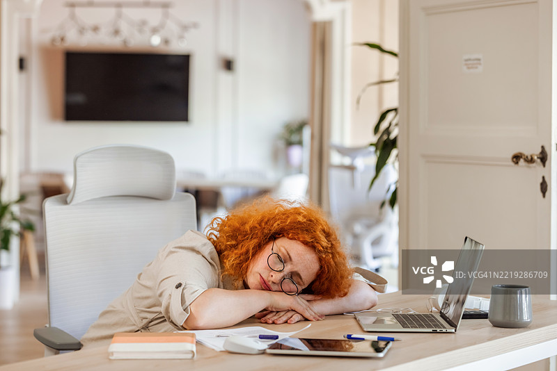 疲惫的女商人在现代办公室环境中桌上小憩图片素材