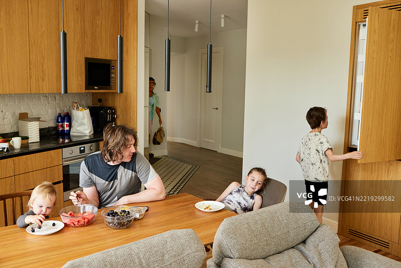 家人在现代厨房里吃水果，祖母回到家中。图片素材