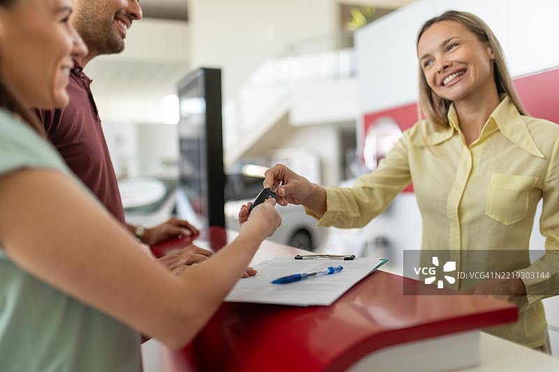 一位汽车销售员正在帮助一对夫妇在展厅签署合同。图片素材