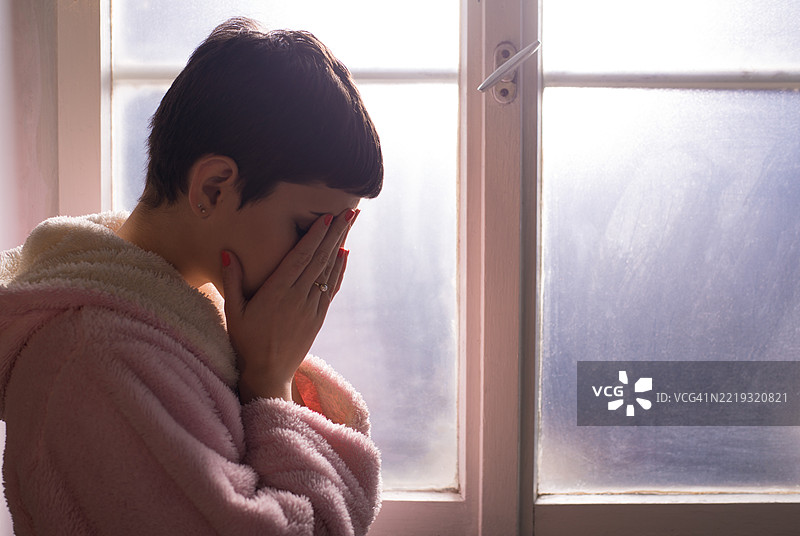 年轻女性癌症患者在医院窗边哭泣图片素材